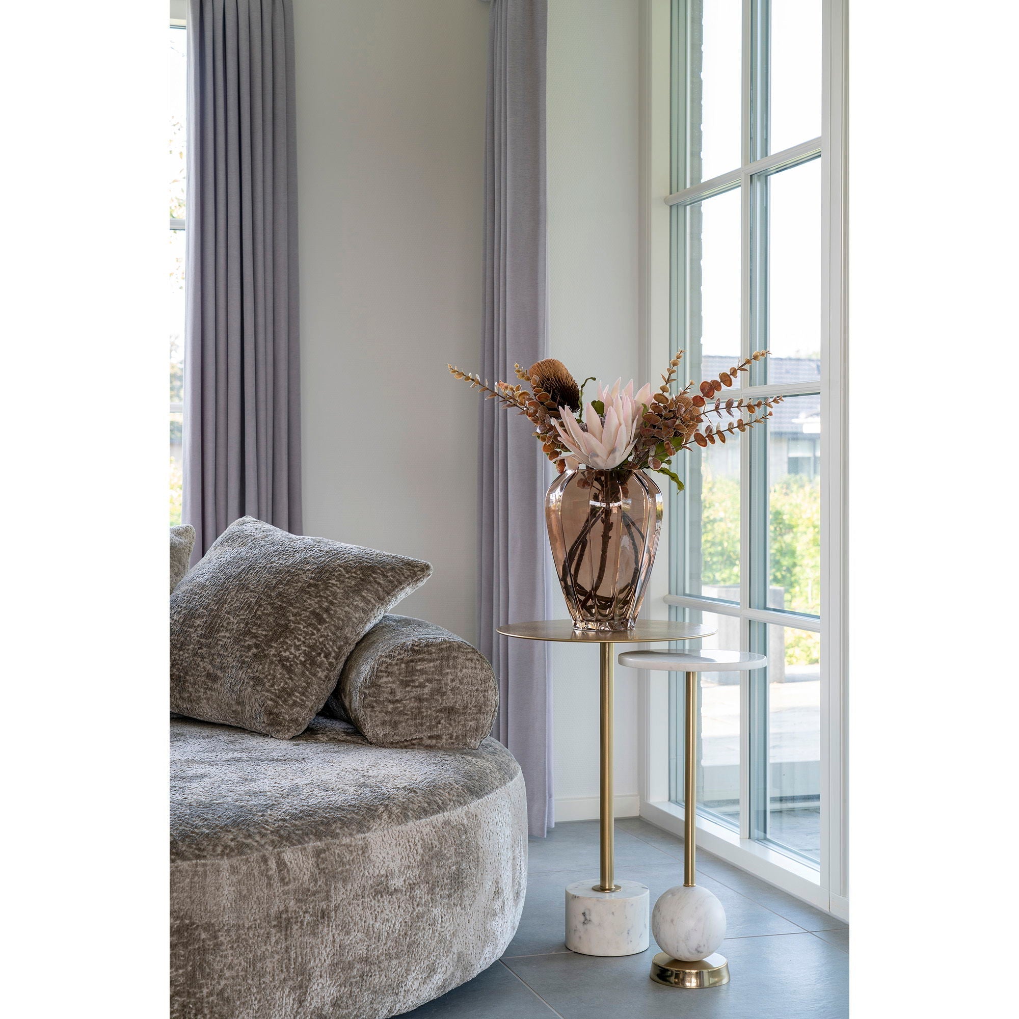 Slank duo van House Nordic Salo tafels met marmer en messing, gestyled met bruin glasvaas en rooswit takboeket bij sofa